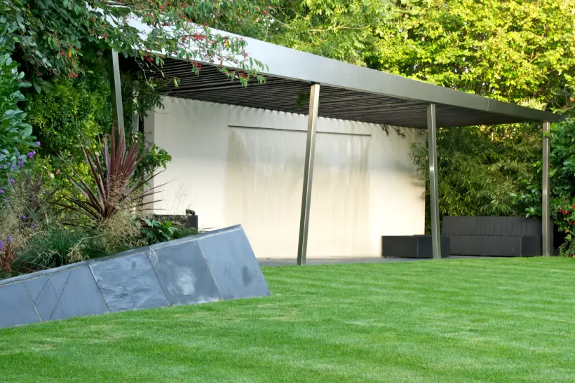 a slanted pergola with a slatted roof housing a water feature