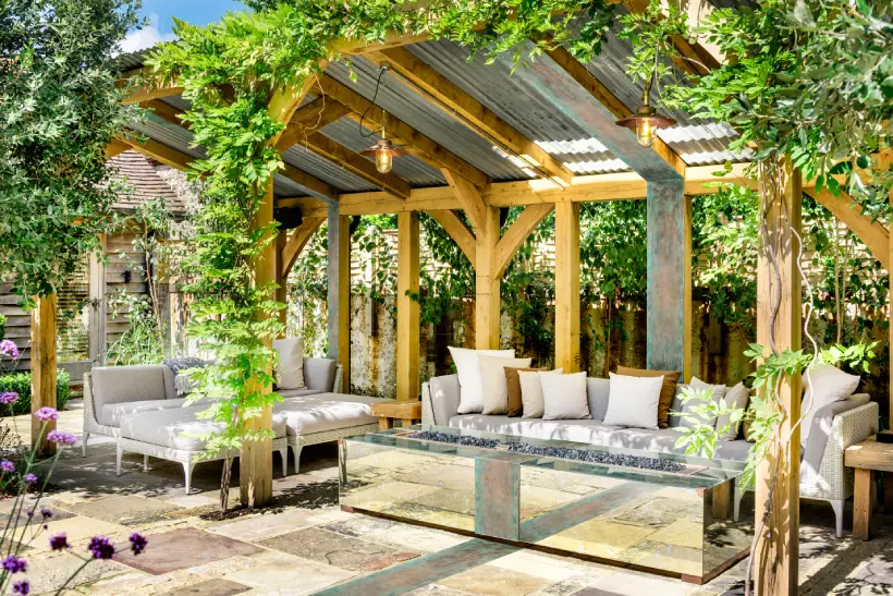 outdoor pergola covered in plants, housing an outdoor living space with outdoor seating and a fireplace