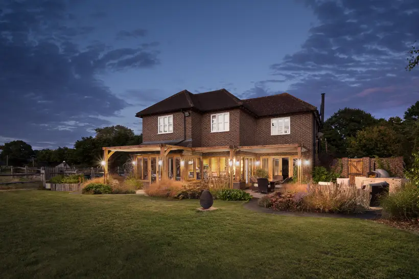 a sectional wooden pergola with lights housing an outdoor seating area as well as an entranceway 