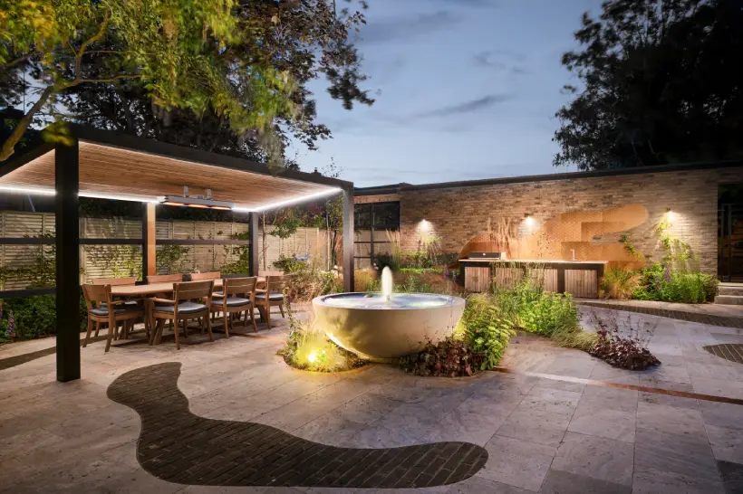 a steel pergola housing an outdoor seating area, lit by two sets of outdoor lighting
